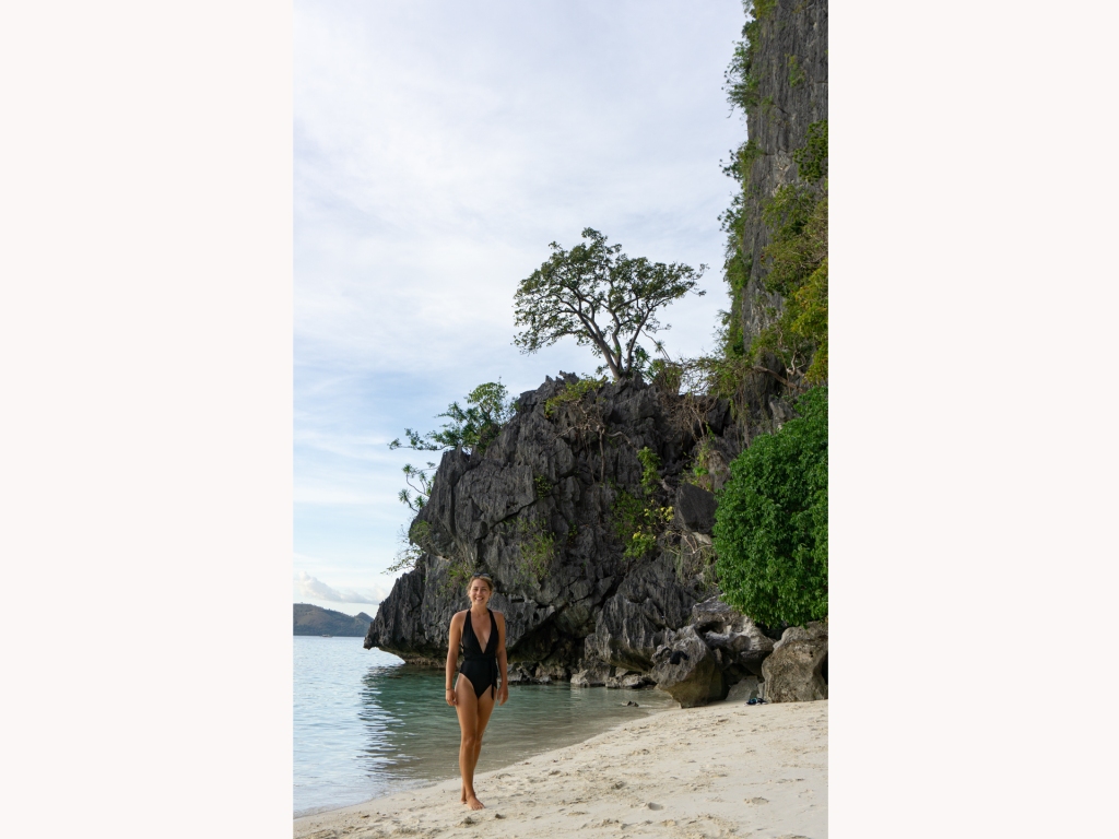 A woman standing on a beach with large limestone cliffs behind her in Coron, Palawan, Philippines.