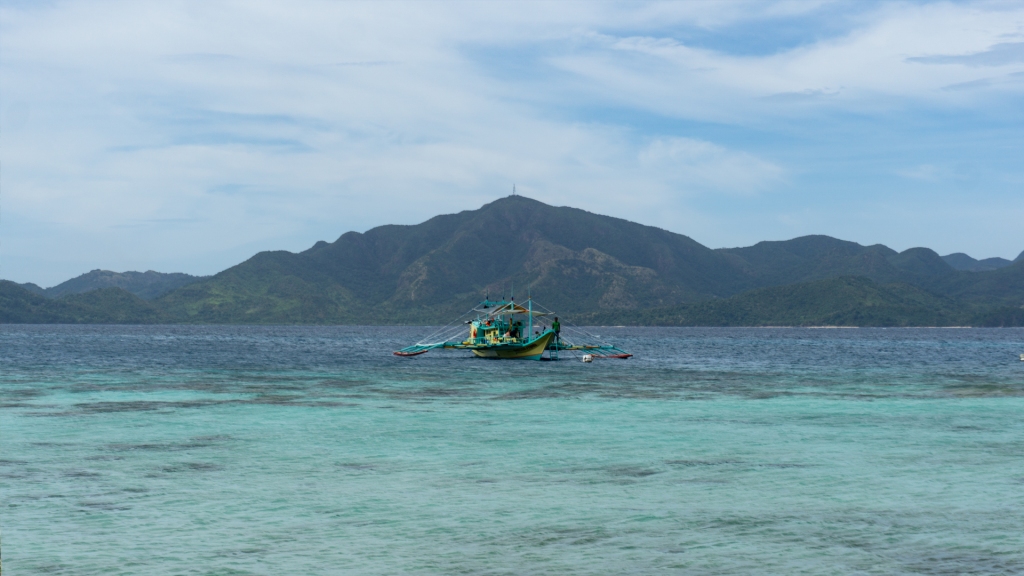 A boat in the center of the ocean and a mountain behind in Coron, Philippines.