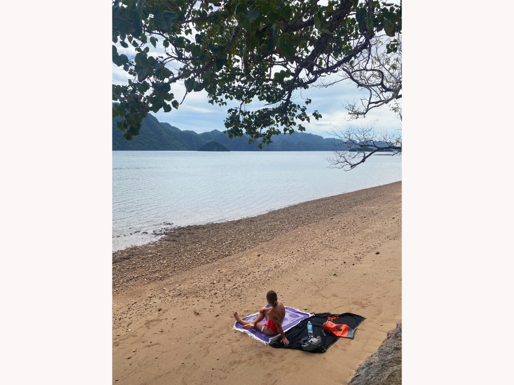 A woman sitting on a beach looking out at the water and mountains in Coron, Palawan, Philippines.