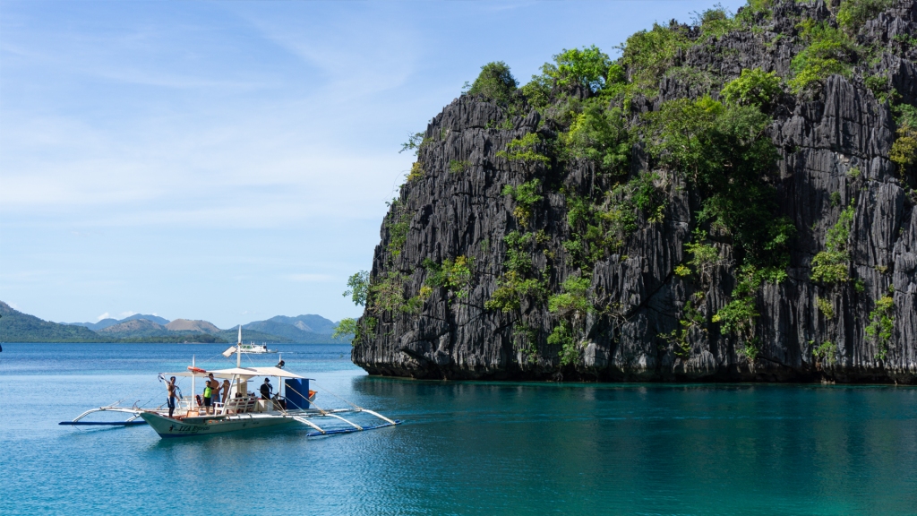 A boat sitting in front of a large limestone cliff in Coron, Palawan, Philippines.