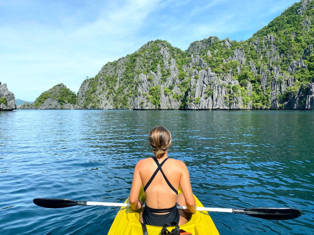 A woman kayaking towards limestone cliffs in the ocean in Coron, Philippines.