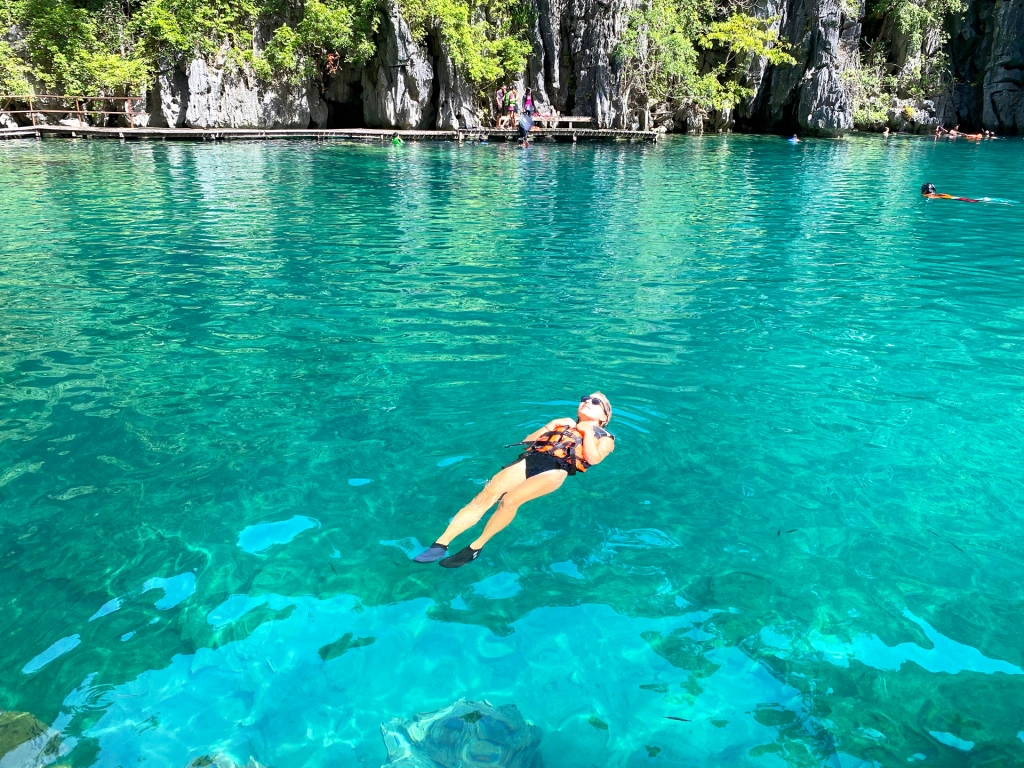 A woman floating with a life jacket in a bright blue lake Kayangan in Coron, Philippines.