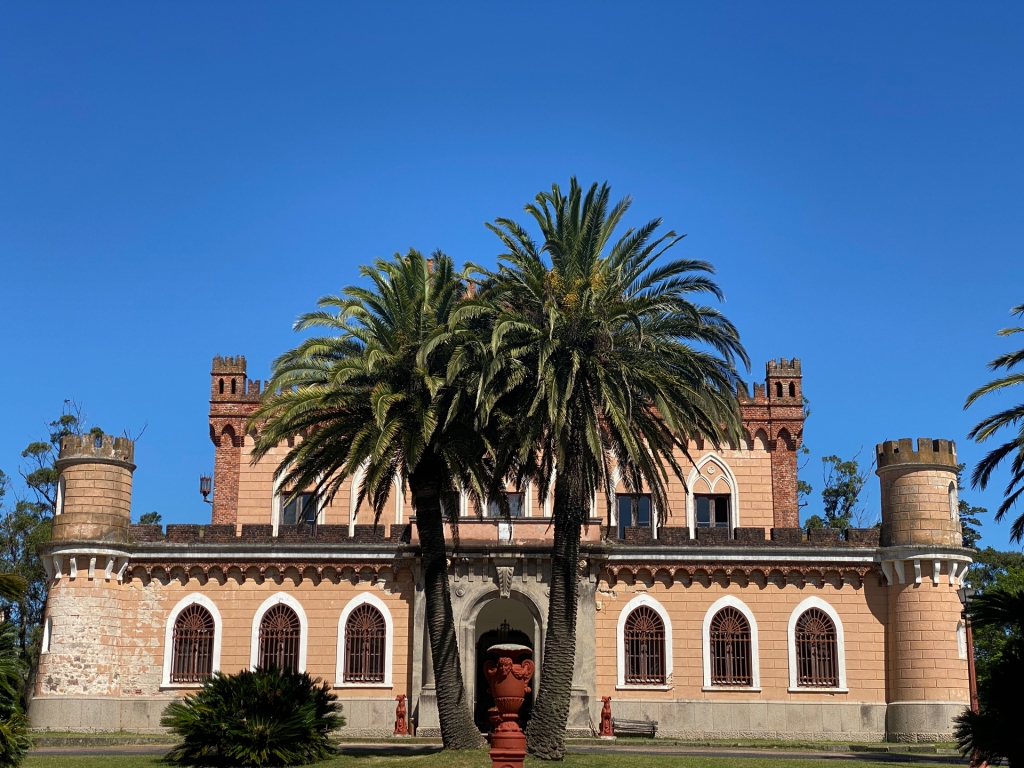 A castle in Uruguay with two large palm trees in the front of the entrance.