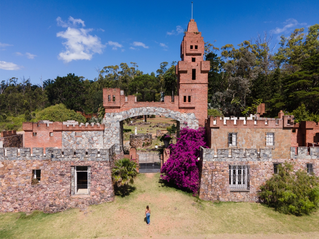 A woman standing in front of the entrance of a large orange brick castle in Uruguay.